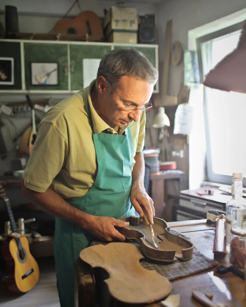 Manos trabajando la madera de un instrumento de cuerda sobre el banco de un taller de lutería